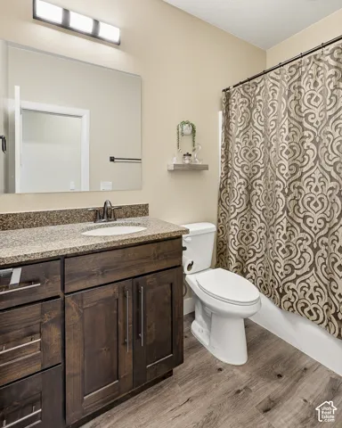 Bathroom featuring a dark wood-finish vanity with an undermount sink, a speckled countertop, and wood-finish flooring
