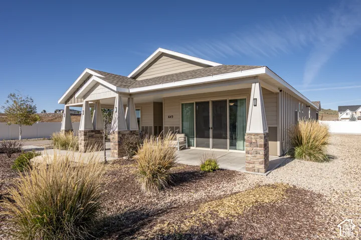 Single-story property featuring a covered front entry with stone-clad columns, a covered patio with sliding glass doors, and a neutral exterior siding
