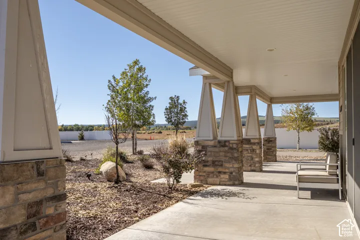 Covered front porch with stone-clad columns, recessed lighting, and a concrete surface