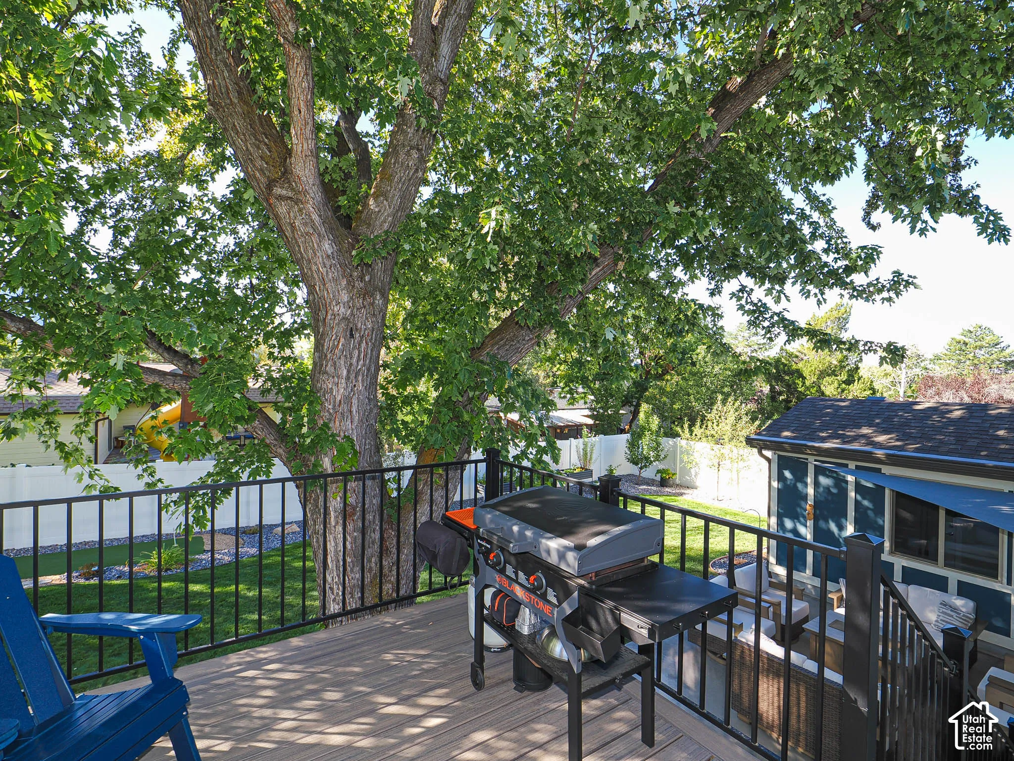 Expansive wood-finish deck with black metal railings, mature trees, and a manicured lawn