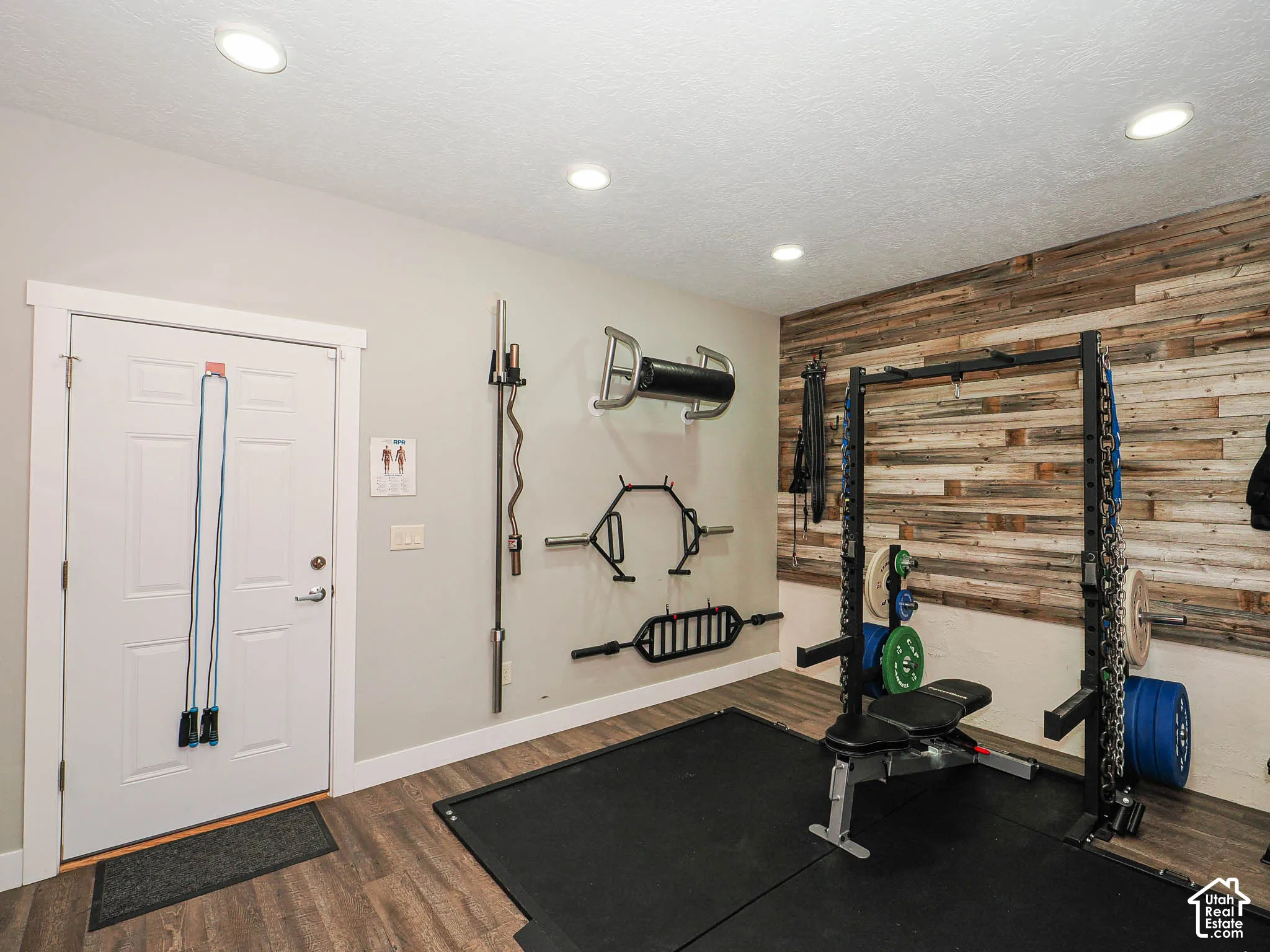 Wood-finish flooring, recessed ceiling lighting, light gray wall paint, and a wood plank accent wall
