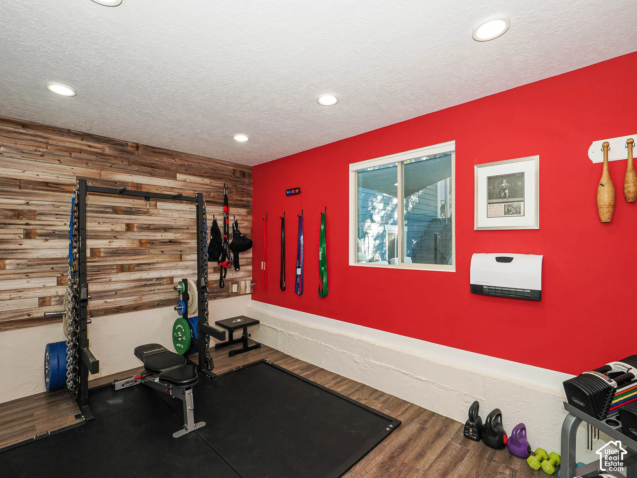 Recessed ceiling lighting, wood-finish flooring, accent wall with horizontal wood paneling, white window frame, and a wall-mounted heating unit