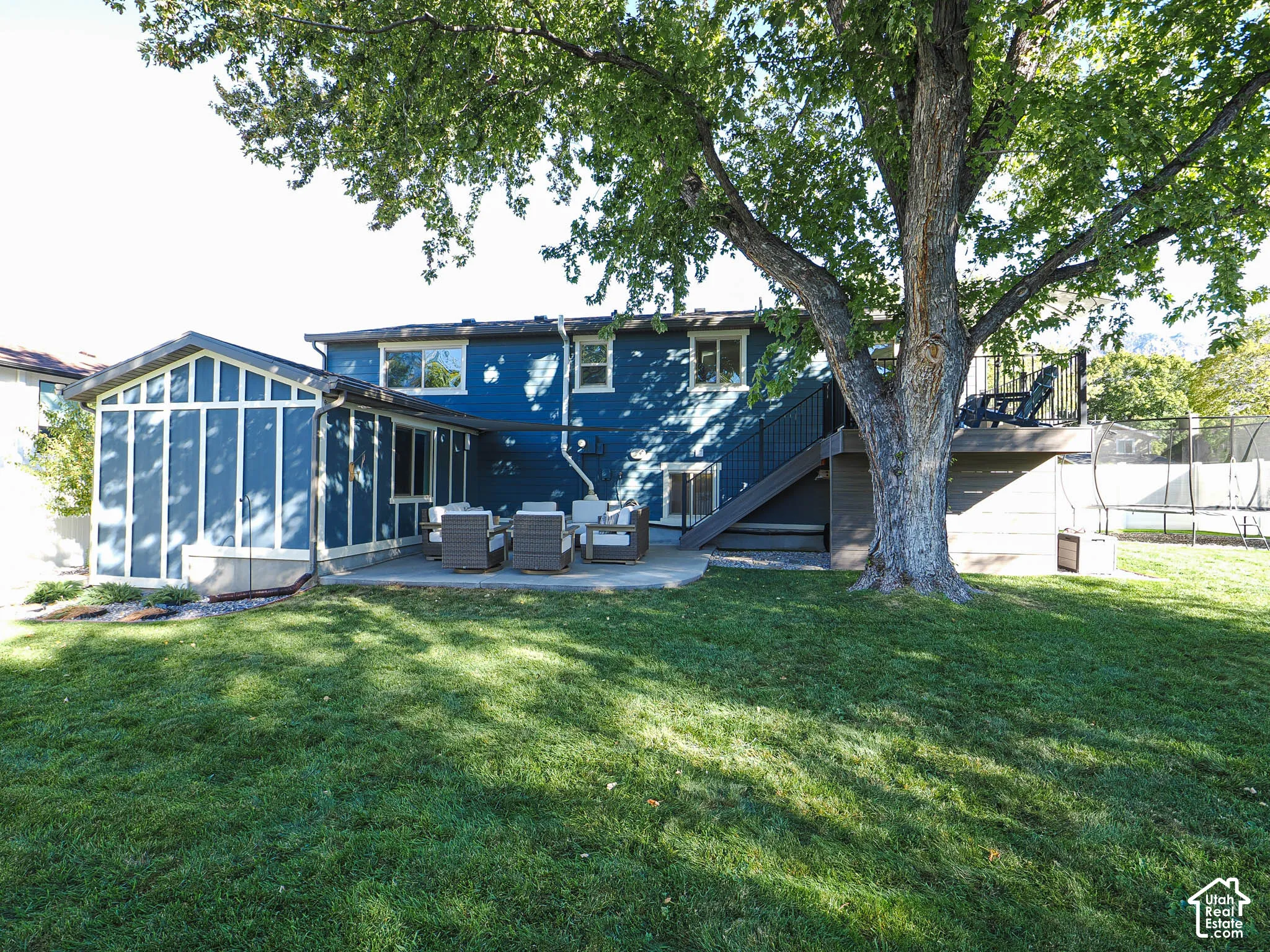 Expansive lawn area with a large mature tree, concrete patio, and enclosed sunroom addition