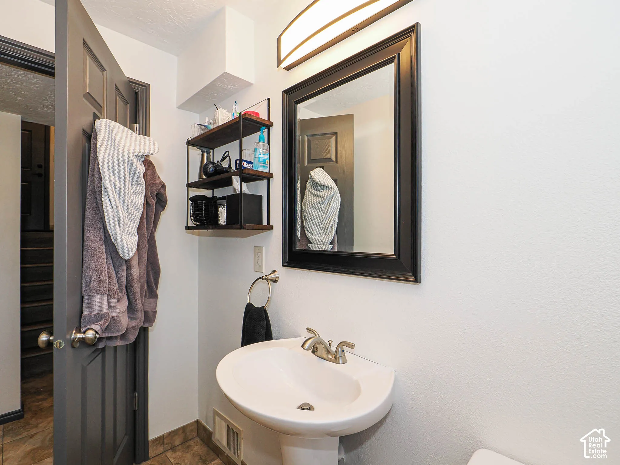 Pedestal sink with a brushed nickel faucet, framed mirror, and a wall-mounted shelving unit