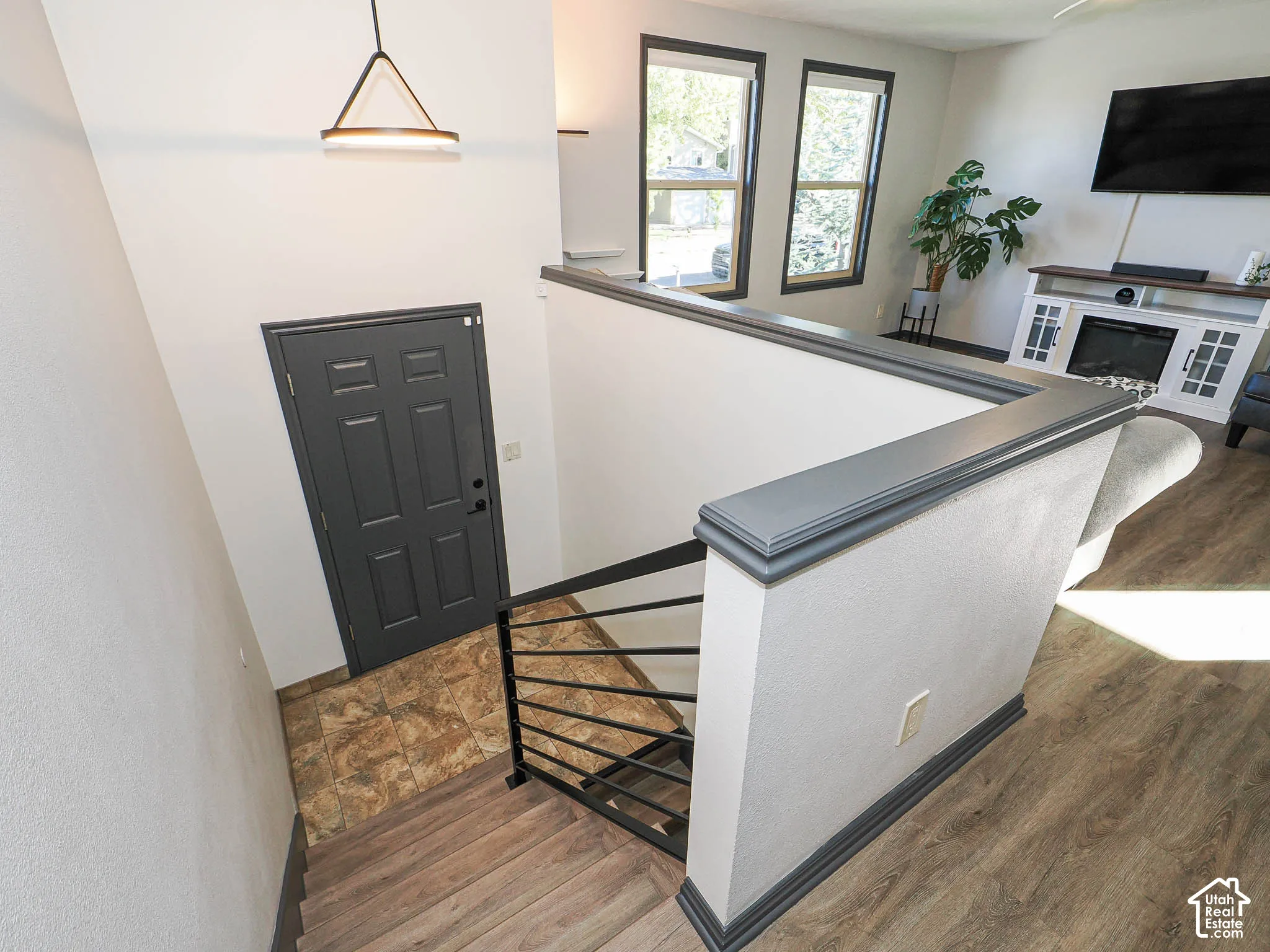Wood-finish flooring, staircase with metal railings, contemporary ceiling light fixture, framed windows, and a built-in media console with fireplace feature