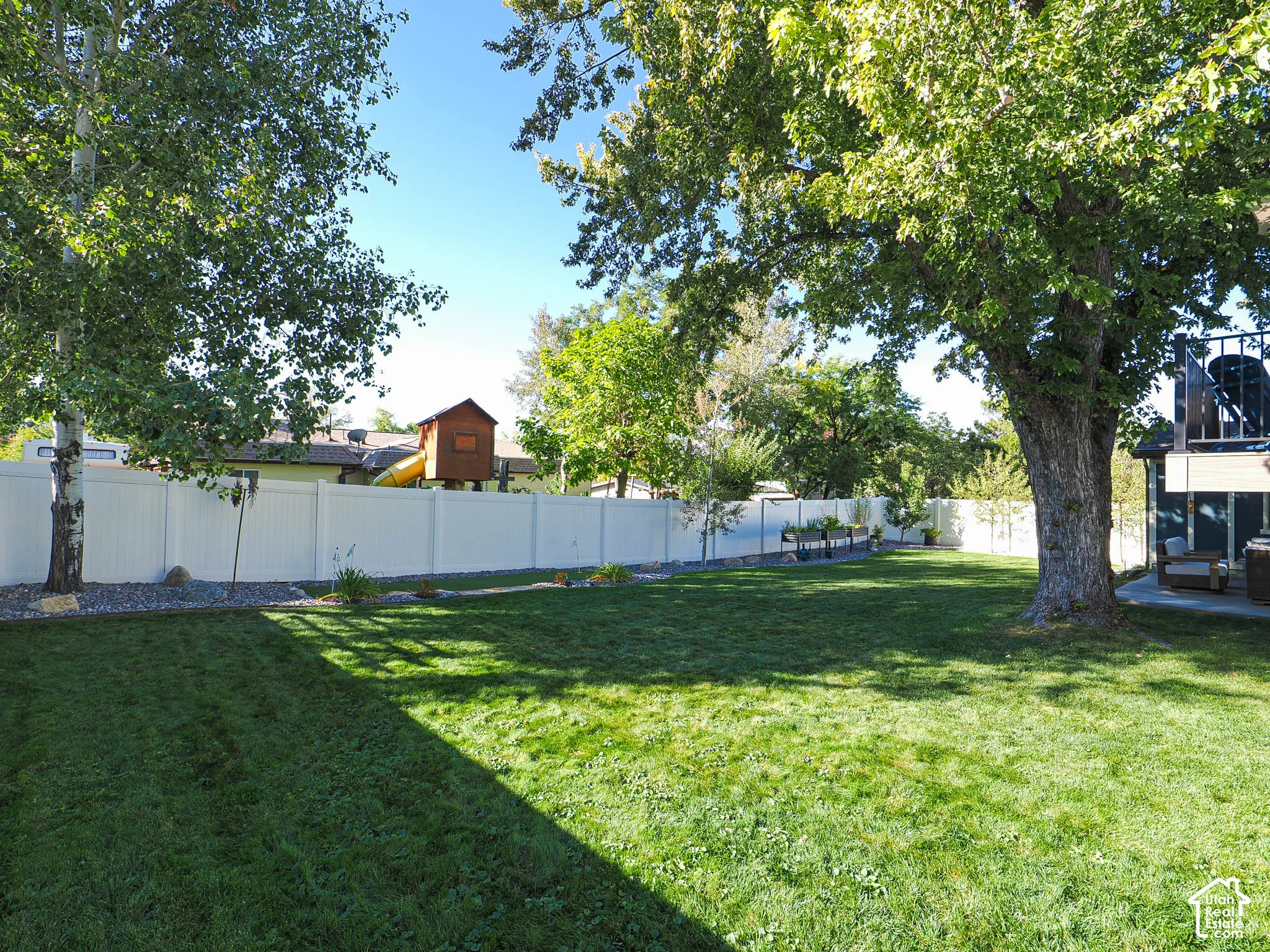 Expansive lawn area with mature trees, surrounded by a white privacy fence