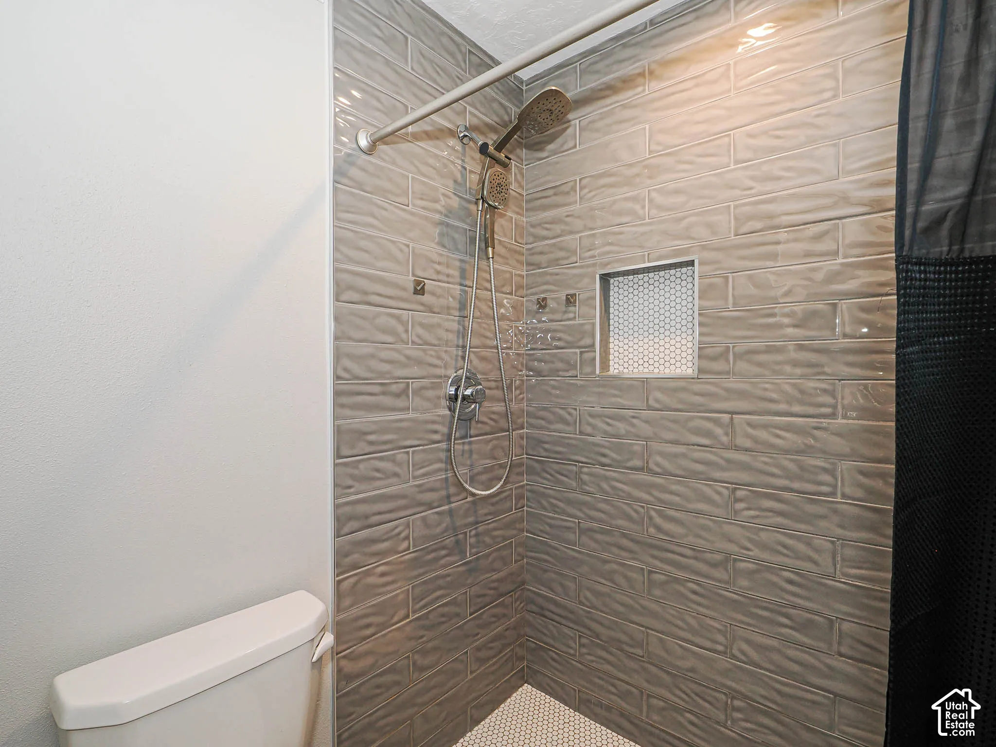 Shower featuring textured subway tile, built-in recessed niche with mosaic accent, and a handheld showerhead