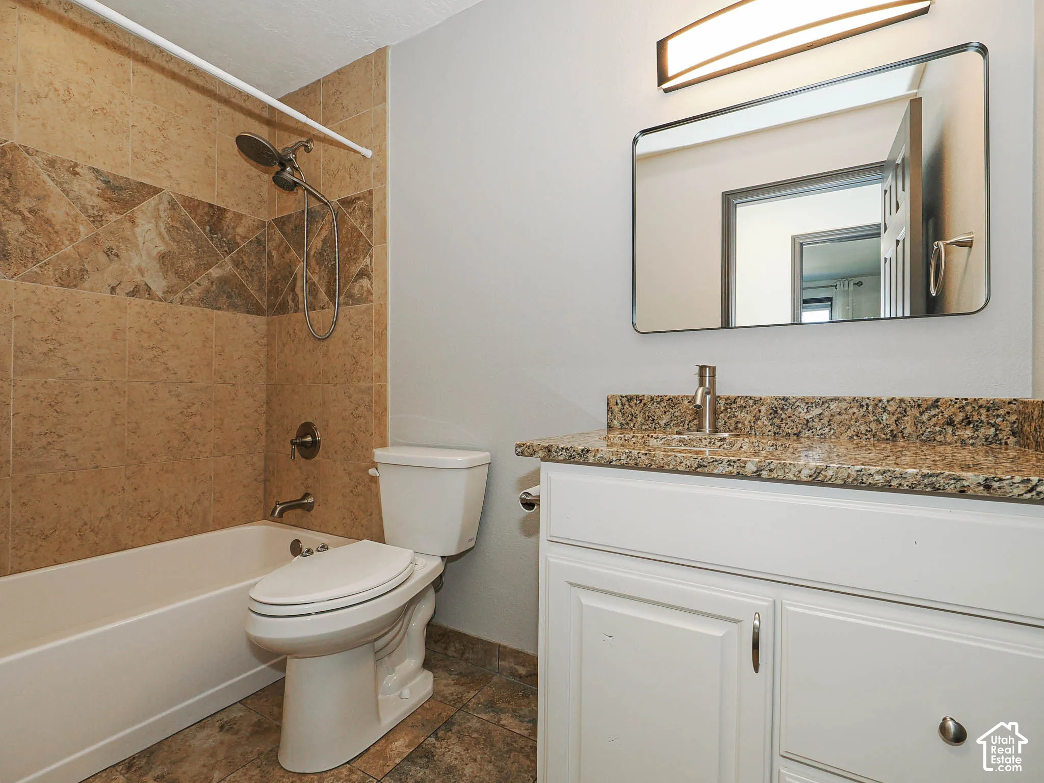Tile flooring, built-in tub with tile surround, white vanity cabinetry with a stone countertop, and an integrated rectangular sink