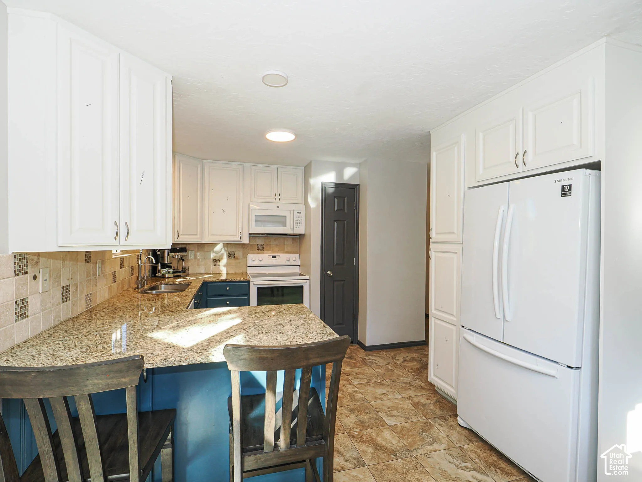 White upper cabinetry, light-toned countertops, white appliances, and tiled flooring