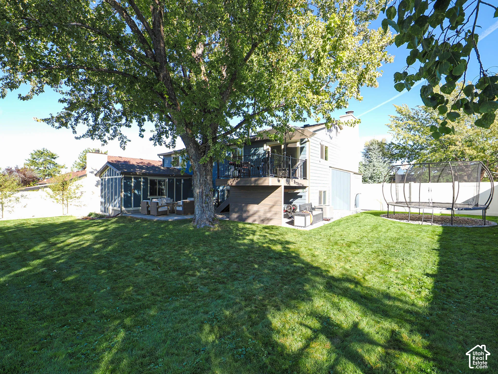 Expansive backyard featuring a large mature tree, manicured lawn, screened-in patio, and a second-story balcony