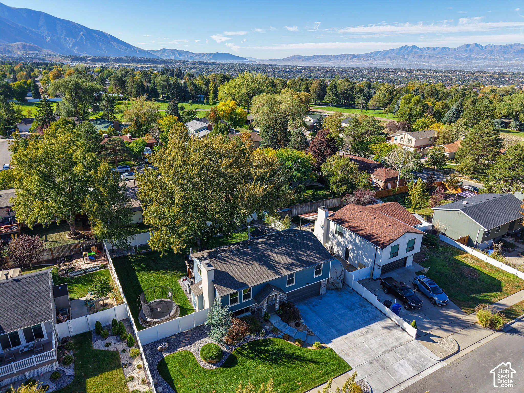 Expansive mountain backdrop, established neighborhood setting, mature trees, concrete driveway, and a fenced backyard