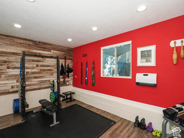 Recessed ceiling lighting, wood-finish flooring, accent wall with horizontal wood paneling, white window frame, and a wall-mounted heating unit