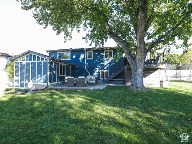 Expansive lawn area with a large mature tree, concrete patio, and enclosed sunroom addition