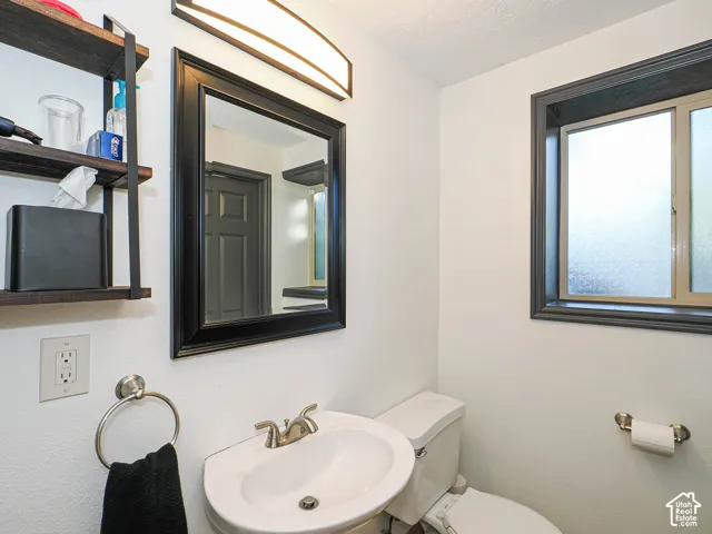 Pedestal sink with brushed nickel faucet, framed mirror with integrated lighting, built-in shelving, and frosted glass window