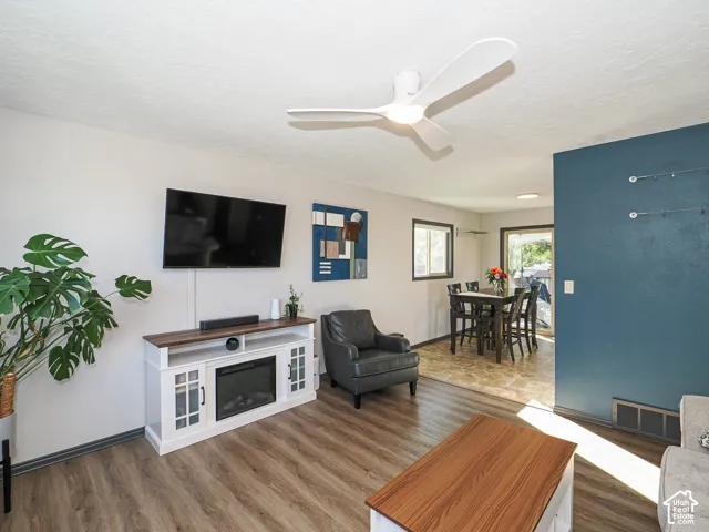 Living area featuring wood-finish flooring, a contemporary ceiling fan with integrated lighting, and a built-in media console with an electric fireplace