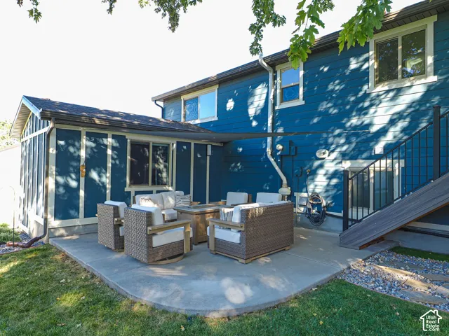 Concrete patio with a sunshade, featuring a partial enclosure with a shingled roof, and exterior stairs with dark railings