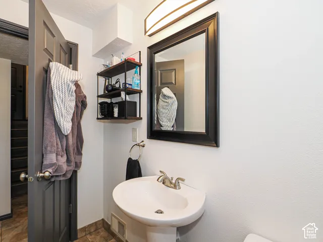 Pedestal sink with a brushed nickel faucet, framed mirror, and a wall-mounted shelving unit