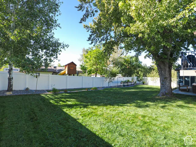 Expansive lawn area with mature trees, surrounded by a white privacy fence