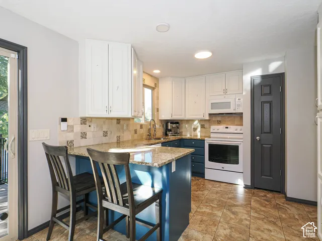 Kitchen featuring two-tone cabinetry, a patterned tile backsplash, granite countertops, tile flooring, and recessed lighting