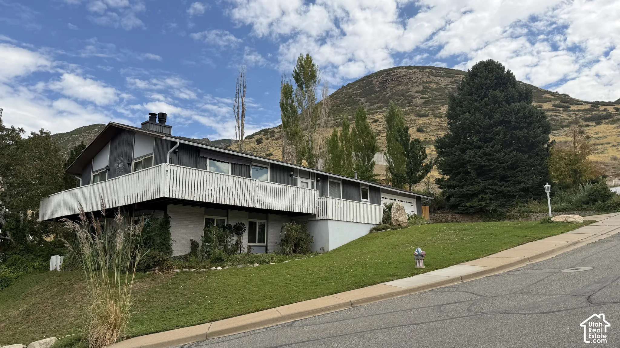Expansive wraparound deck, situated on manicured grounds featuring mature landscaping and mature trees