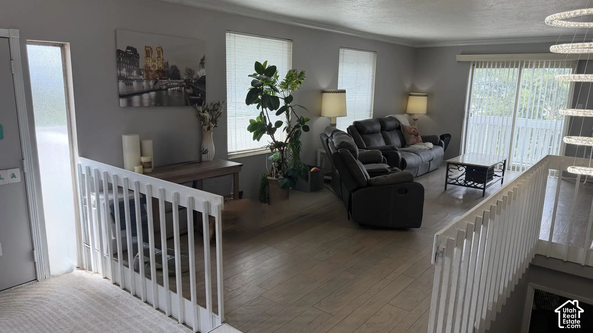 Open-concept living area featuring wood-finish flooring, white railing, and a sliding glass door