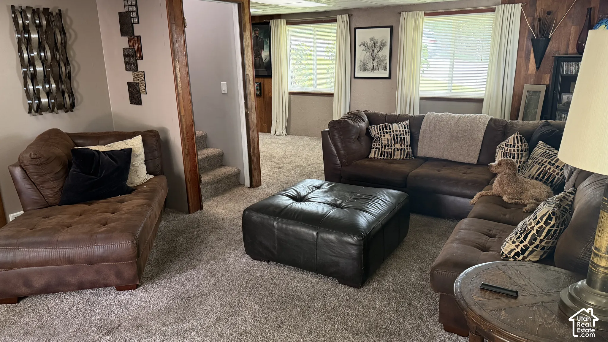 Spacious recreation room featuring neutral carpeting, multiple windows with natural light, and wood-beam accents throughout the space