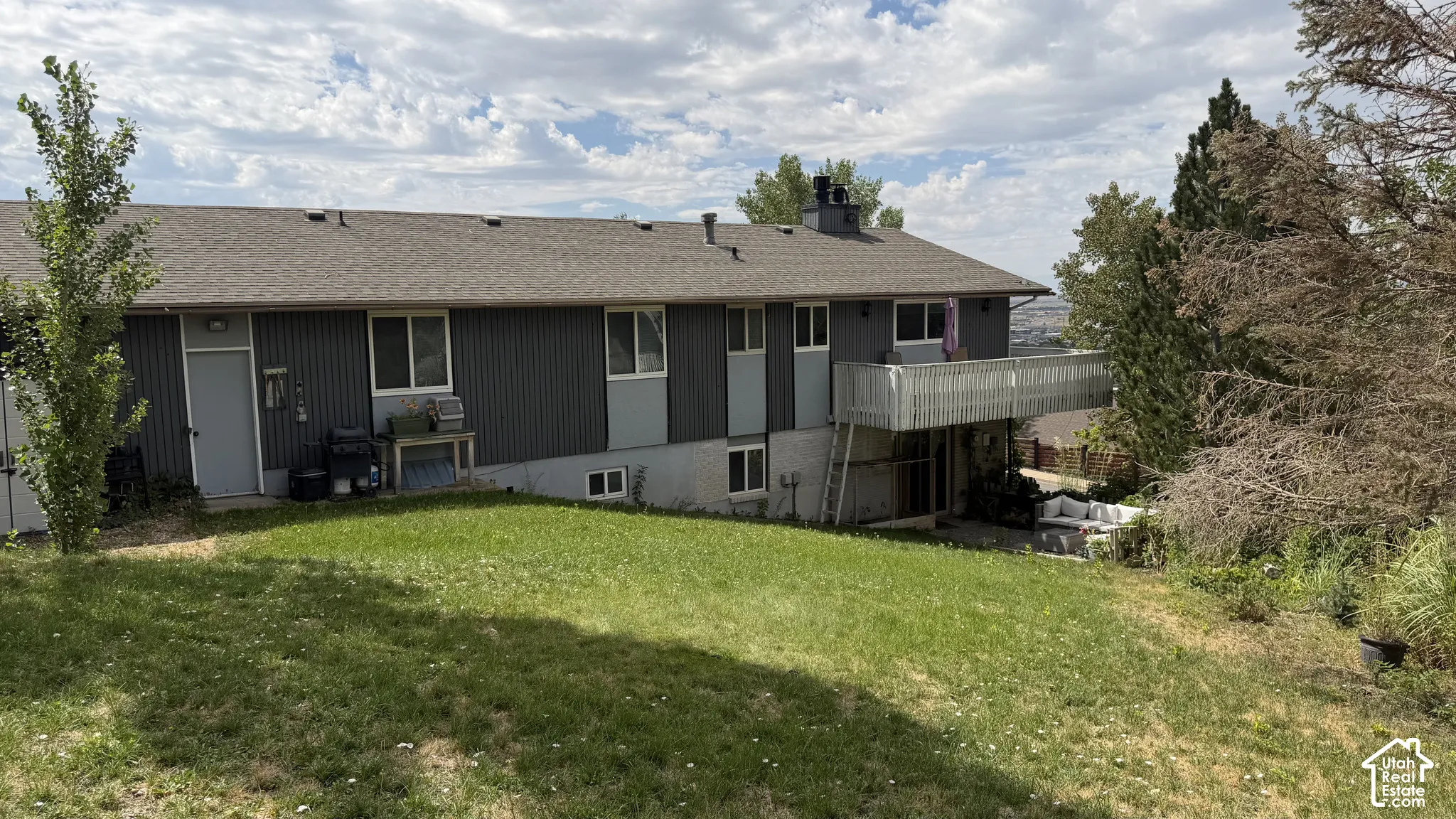 Spacious residential home featuring a modern dark-finish exterior with multiple entry points, expansive manicured lawn with mature landscaping, and a multi-level deck structure providing outdoor living space