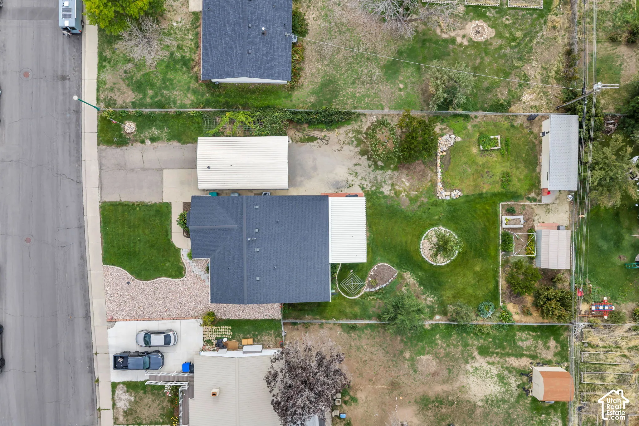 Expansive lot featuring a main residence with a dark shingle roof, a detached garage with a light-colored roof, a gravel parking area, and a large grass lawn