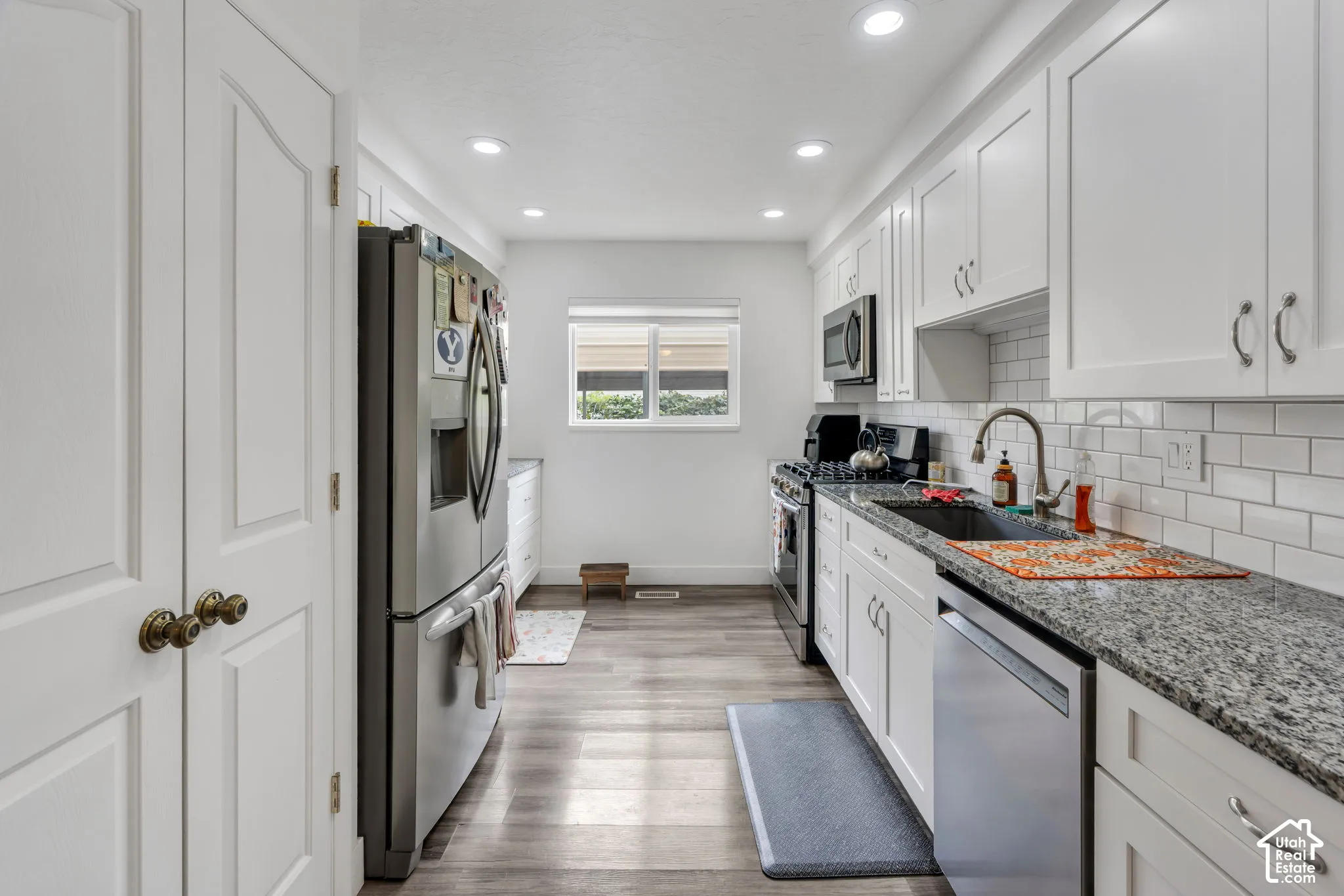 Galley kitchen featuring white cabinetry, gray wood-finish flooring, granite countertops, and stainless steel appliances