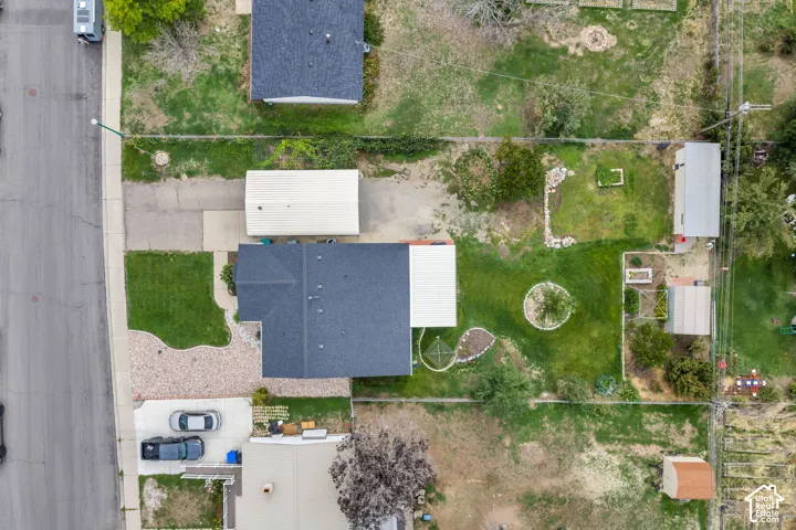 Expansive lot featuring a main residence with a dark shingle roof, a detached garage with a light-colored roof, a gravel parking area, and a large grass lawn