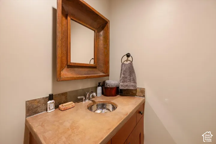Wood-framed mirror, integrated basin, stone countertop, tile backsplash, and wood cabinetry