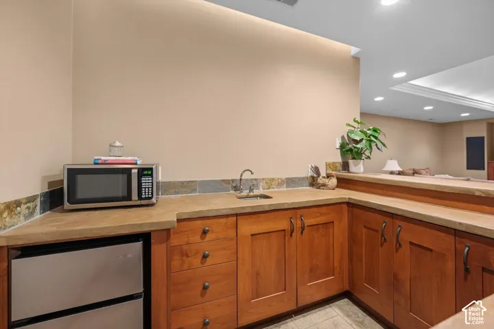 Wet bar featuring wood-finish cabinetry, stone countertops, and a stainless steel under-counter refrigerator