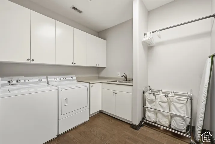 White upper and lower cabinetry, wood-finish flooring, undermount sink with a chrome faucet, and a built-in hanging rod