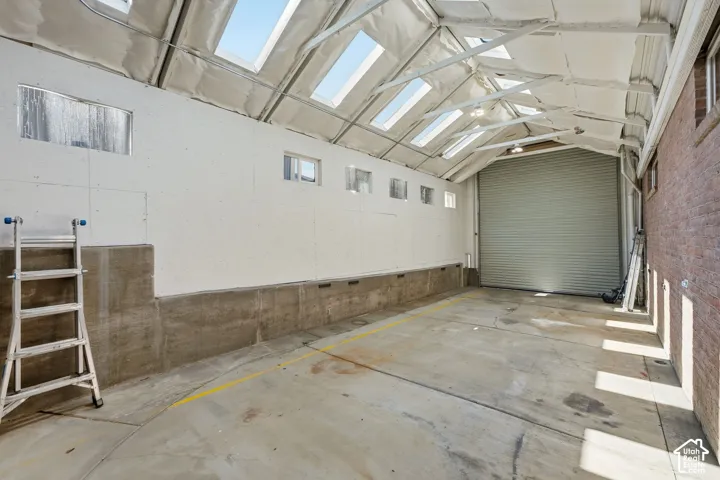 Spacious interior with a roll-up door, skylights, concrete flooring, and exposed brick wall
