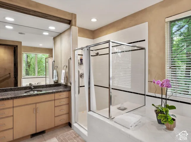Bathroom featuring a glass-enclosed shower, built-in bathtub, dual-sink vanity with granite countertop, and wood-finish cabinetry