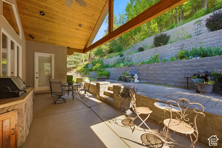 Covered patio featuring a wood-finished ceiling, exposed beams, and an outdoor cooking station with stone-finish base