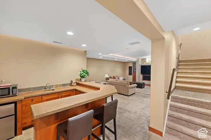 Full-service wet bar featuring wood cabinetry, stone-finish countertops, and a tiled backsplash