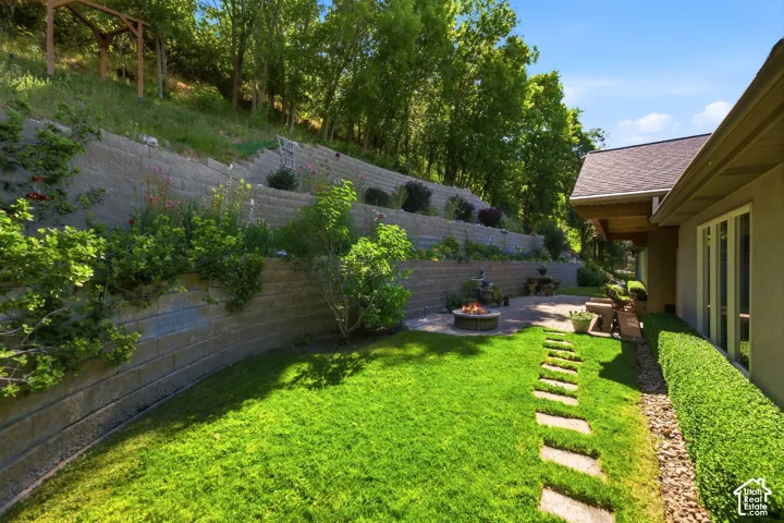 Expansive terraced retaining walls, concrete paver patio, integrated fire pit, and stone pathway