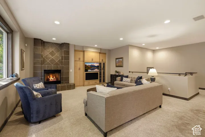 Stone-clad fireplace with hearth, built-in media center with cabinetry, recessed lighting, and carpet flooring