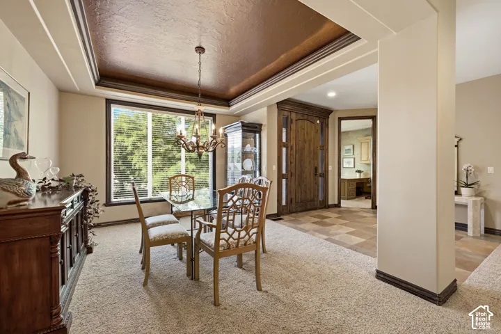 Recessed ceiling with an ornamental chandelier, large window with blinds, wood-finish flooring, and a decorative wood-paneled door
