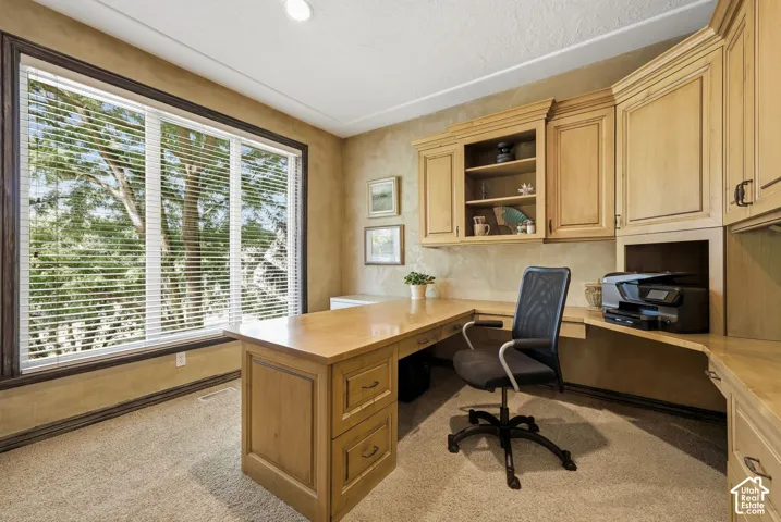 Built-in desk with wood-finish cabinetry, integrated shelving, and large window with blinds
