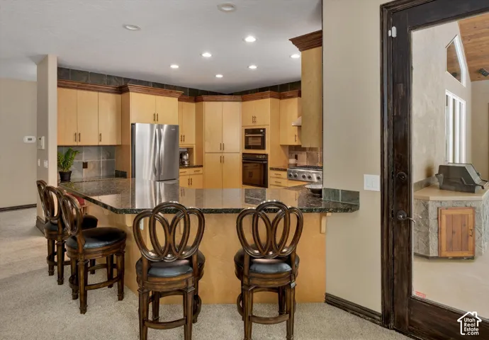 Kitchen featuring light wood cabinetry, dark stone countertops, stainless steel appliances, and recessed lighting