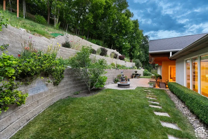 Expansive terraced landscaping with mature plantings, a paver patio, and a stone-stepped pathway, complemented by an exterior featuring large windows