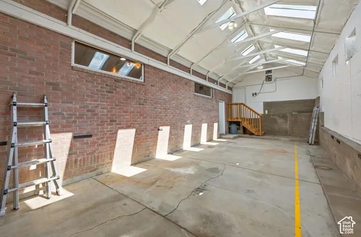 Exposed brick wall, concrete flooring, skylights, pitched ceiling, and wood-finish staircase