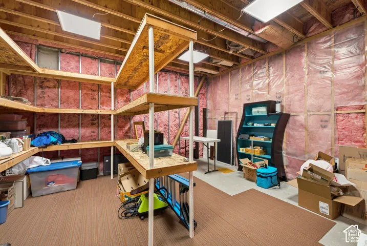 Unfinished basement with exposed ceiling joists and wall insulation, featuring built-in wooden shelving and recessed lighting