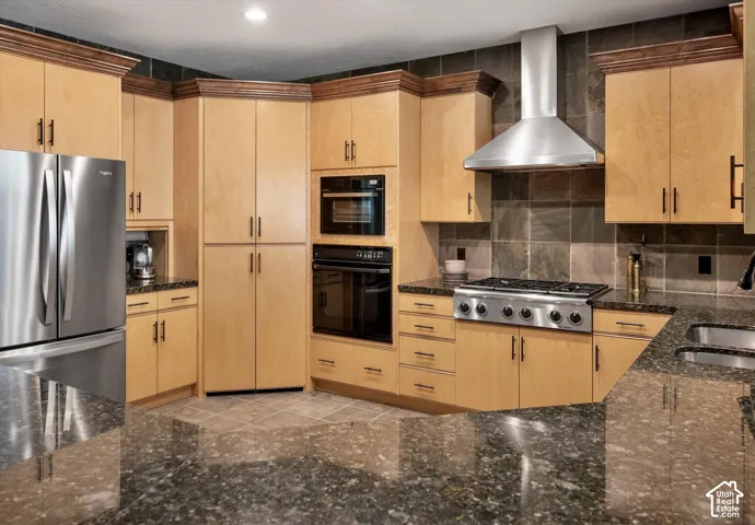Kitchen with light wood-finish cabinetry, dark stone countertops, stainless steel appliances, and a tiled backsplash