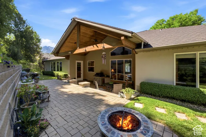Expansive paver patio with a built-in fire pit, covered outdoor living area featuring a wood-beam ceiling, and large windows