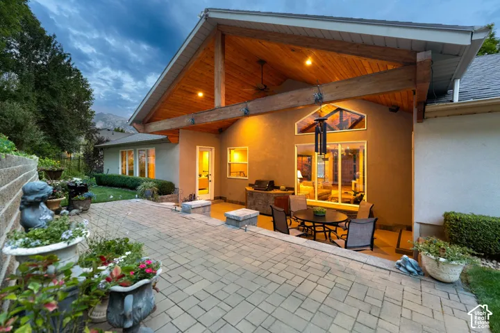 Expansive paved patio featuring an exposed beam vaulted ceiling with recessed lighting, a built-in outdoor kitchen, and large windows