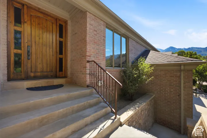 Brick exterior with a paneled wood entry door, sidelight windows, and an ornate metal handrail leading to the entrance