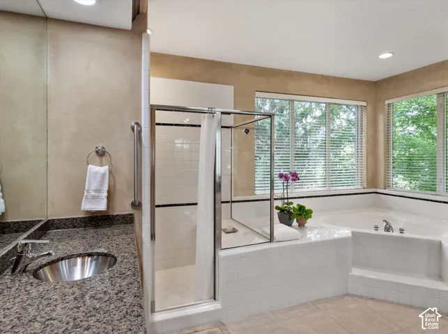 Bathroom featuring a built-in soaking tub, separate glass-enclosed shower with white tile, vanity with a polished chrome faucet and undermount sink, and large windows with blinds